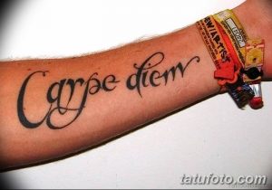 Фото татуировки 'Carpe Diem' на предплечье, выполненной классическим шрифтом. Черно-белый рисунок с четкими линиями.