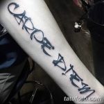 Фото татуировки 'Carpe Diem' на предплечье, выполненной в стиле brush lettering. Неровные, динамичные линии создают эффект рукописного текста.