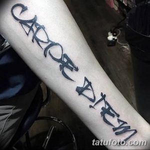 Фото татуировки 'Carpe Diem' на предплечье, выполненной в стиле brush lettering. Неровные, динамичные линии создают эффект рукописного текста.