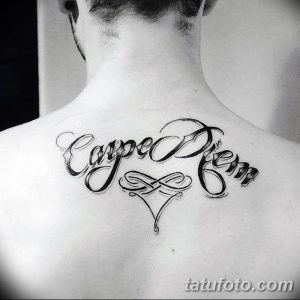 Фотография татуировки 'Carpe Diem' на спине, выполненной изящным шрифтом с декоративными элементами. Черно-белый рисунок с плавными линиями.