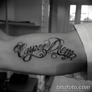 Черно-белое фото татуировки 'Carpe Diem' на руке. Изящный шрифт с тонкими линиями и завитушками, создающий элегантный и стильный вид.