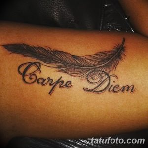 Фото тату: надпись 'Carpe Diem' с изображением пера на спине женщины. Черно-серые тона, реалистичная проработка пера.