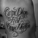 Фото тату: изящная черно-белая каллиграфическая надпись 'Carpe Diem feat Carpe Hodiem' на боку мужчины. Декоративные завитки и узоры.