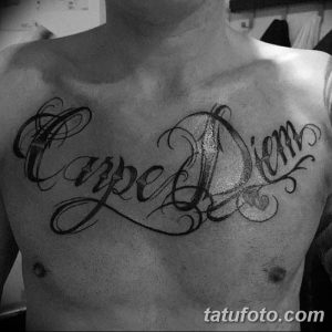 Фото тату: большая черно-белая татуировка 'Carpe Diem' на груди мужчины. Изящный каллиграфический шрифт и декоративные элементы.