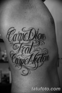 Фото тату: изящная черно-белая каллиграфическая надпись 'Carpe Diem feat Carpe Hodiem' на боку мужчины. Декоративные завитки и узоры.