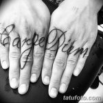 Фото татуировки 'Carpe Diem', разделенной между пальцами рук. Минималистичный рисунок татуировки черными чернилами.
