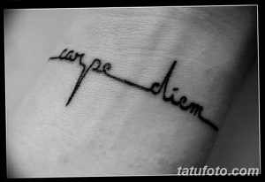 Фото минималистичной татуировки 'Carpe Diem' на запястье, выполненной тонкими черными линиями. Изящный рисунок татуировки.