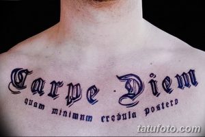 Фото тату надписи 'Carpe Diem' на груди мужчины, выполненной черными чернилами в готическом стиле. Детализированный рисунок татуировки.