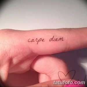 Фото минималистичной татуировки с надписью 'Carpe Diem' на пальце, выполненной тонкими черными линиями. Нежный и изящный дизайн.
