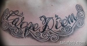 Фото тату надписи 'Carpe Diem' с витиеватыми узорами и завитушками, выполненной черными чернилами. Красивый и оригинальный дизайн.
