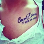 Фото тату надписи 'Carpe Diem' с римскими цифрами на груди девушки, выполненной черными чернилами. Классический и вдохновляющий рисунок.