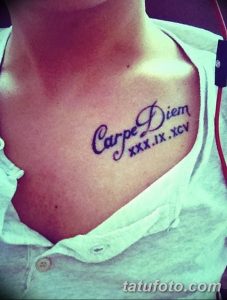 Фото тату надписи 'Carpe Diem' с римскими цифрами на груди девушки, выполненной черными чернилами. Классический и вдохновляющий рисунок.