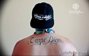 Фото тату надписи 'Carpe Diem' выполненной изящным шрифтом на спине. Черно-серая татуировка, тонкие линии, элегантный дизайн.