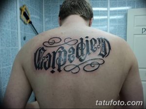 Фото татуировки надписи 'Carpe Diem', выполненной с декоративными завитушками на спине. Черно-белая татуировка.