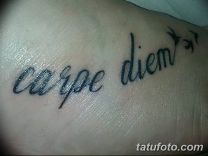 Фото тату надписи 'Carpe Diem' черным цветом, выполненной каллиграфическим шрифтом на внутренней стороне запястья. Минималистичный рисунок татуировки.