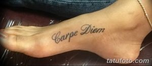 Фото тату надписи 'Carpe Diem' черным цветом, выполненной каллиграфическим шрифтом на верхней части стопы.
