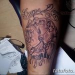 Фото тату на предплечье с изображением тающих часов, черепа и надписи 'Carpe Diem' в черно-серых тонах.