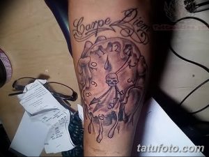 Фото тату на предплечье с изображением тающих часов, черепа и надписи 'Carpe Diem' в черно-серых тонах.
