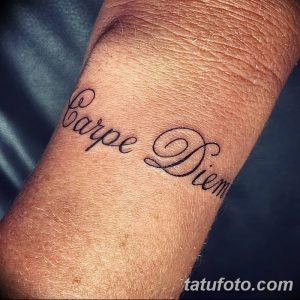 Фото тату надписи 'Carpe Diem' черным цветом, выполненной каллиграфическим шрифтом на внутренней стороне запястья.