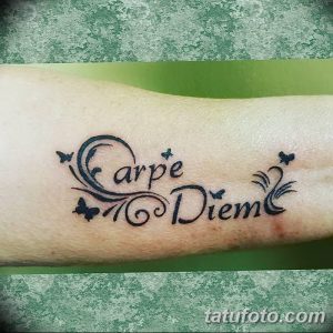 Фото тату надписи 'Carpe Diem' с изображением бабочек на запястье. Черно-серая татуировка с нежным дизайном и изящными линиями.