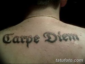 Фото тату надписи 'Carpe Diem' готическим шрифтом на спине, между лопатками. Черно-серая татуировка с выразительными линиями и завитками.