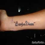 Фото тату надписи 'Carpe Diem' черным цветом на внутренней стороне запястья. Минималистичный рисунок татуировки, выполненный четким шрифтом.