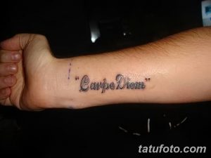 Фото тату надписи 'Carpe Diem' черным цветом на внутренней стороне запястья. Минималистичный рисунок татуировки, выполненный четким шрифтом.
