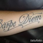 Фото тату надписи 'Carpe Diem' на предплечье. Черный контур, каллиграфический шрифт, классический дизайн. Подходит для тех, кто ценит простоту и элегантность.