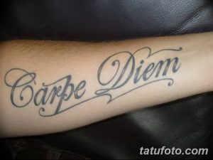 Фото тату надписи 'Carpe Diem' на предплечье. Черный контур, каллиграфический шрифт, классический дизайн. Подходит для тех, кто ценит простоту и элегантность.