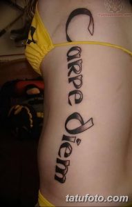 Фото тату надписи 'Carpe Diem', выполненной вертикально на боку. Черный цвет, крупный шрифт, привлекающий внимание дизайн. Подходит для смелых личностей.