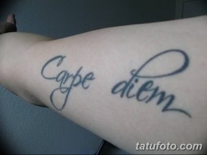 Фото тату надписи 'Carpe Diem' на предплечье. Черный контур, каллиграфический шрифт, изящный дизайн. Подходит для тех, кто ценит минимализм.