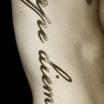 Фото тату с надписью 'Carpe Diem', выполненной вертикально на боку, выглядит изящно и женственно.