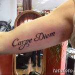 Фото тату с надписью 'Carpe Diem', выполненной классическим шрифтом на предплечье, выглядит стильно и уверенно.