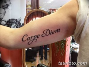 Фото тату с надписью 'Carpe Diem', выполненной классическим шрифтом на предплечье, выглядит стильно и уверенно.