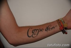 Фото тату с надписью 'Carpe Diem' на предплечье, выполненной простым шрифтом. Классический и минималистичный рисунок татуировки.