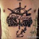 Фото тату на груди с изображением морского руля, розы, ленты с надписью 'Carpe Diem', якоря и кинжалов. Сложный и детализированный рисунок татуировки.