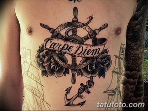 Фото тату на груди с изображением морского руля, розы, ленты с надписью 'Carpe Diem', якоря и кинжалов. Сложный и детализированный рисунок татуировки.