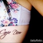 Фото тату с надписью 'Carpe Diem' на женском боку, выполненной красивым шрифтом. Изящный рисунок татуировки.