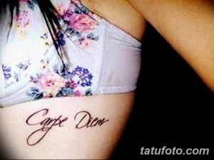 Фото тату с надписью 'Carpe Diem' на женском боку, выполненной красивым шрифтом. Изящный рисунок татуировки.