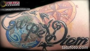 Фото сложной татуировки на плече, включающей надпись 'Carpe Diem', компас, ласточек и другие элементы. Детализированный и красочный рисунок тату.