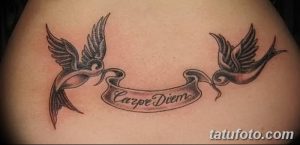 Фото татуировки надписи 'Carpe Diem' на спине, окруженной двумя ласточками, держащими ленту с надписью. Красивый и символичный рисунок тату.
