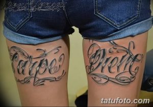 Фото тату надписи "Carpe Diem" на бедрах женщины. Черно-серый рисунок татуировки, выполненный каллиграфическим шрифтом с декоративными элементами.