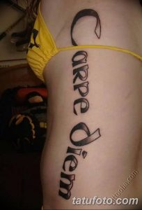 Фото тату надписи "Carpe Diem", расположенной вертикально на боку женщины. Черно-серый рисунок татуировки, выполненный простым шрифтом.