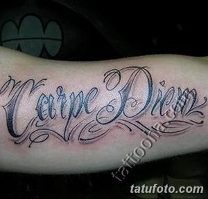 Фото тату надписи "Carpe Diem" с декоративными завитушками на предплечье. Черно-серый рисунок татуировки, выполненный в каллиграфическом стиле.