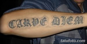 Фото тату надписи "Carpe Diem" на предплечье мужчины. Черно-серый рисунок татуировки, выполненный в готическом стиле.