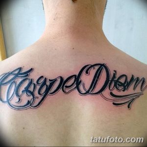 Фотография татуировки с надписью 'Carpe Diem' на спине мужчины. Черный контур, стилизованный шрифт, крупный размер.