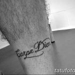 Фотография татуировки с надписью 'Carpe Diem' на икре мужчины. Черный контур, каллиграфический шрифт, лаконичный дизайн.