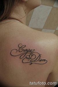 Фотография изящной татуировки с надписью 'Carpe Diem' на спине женщины. Черный контур, каллиграфический шрифт, женственный дизайн.