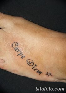 Фотография минималистичной татуировки с надписью 'Carpe Diem' на внешней стороне стопы. Черный контур, аккуратный шрифт, женственная татуировка.