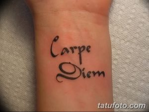 Фото минималистичной татуировки с надписью 'Carpe Diem' на запястье. Черный рисунок татуировки, выполненный простым шрифтом.